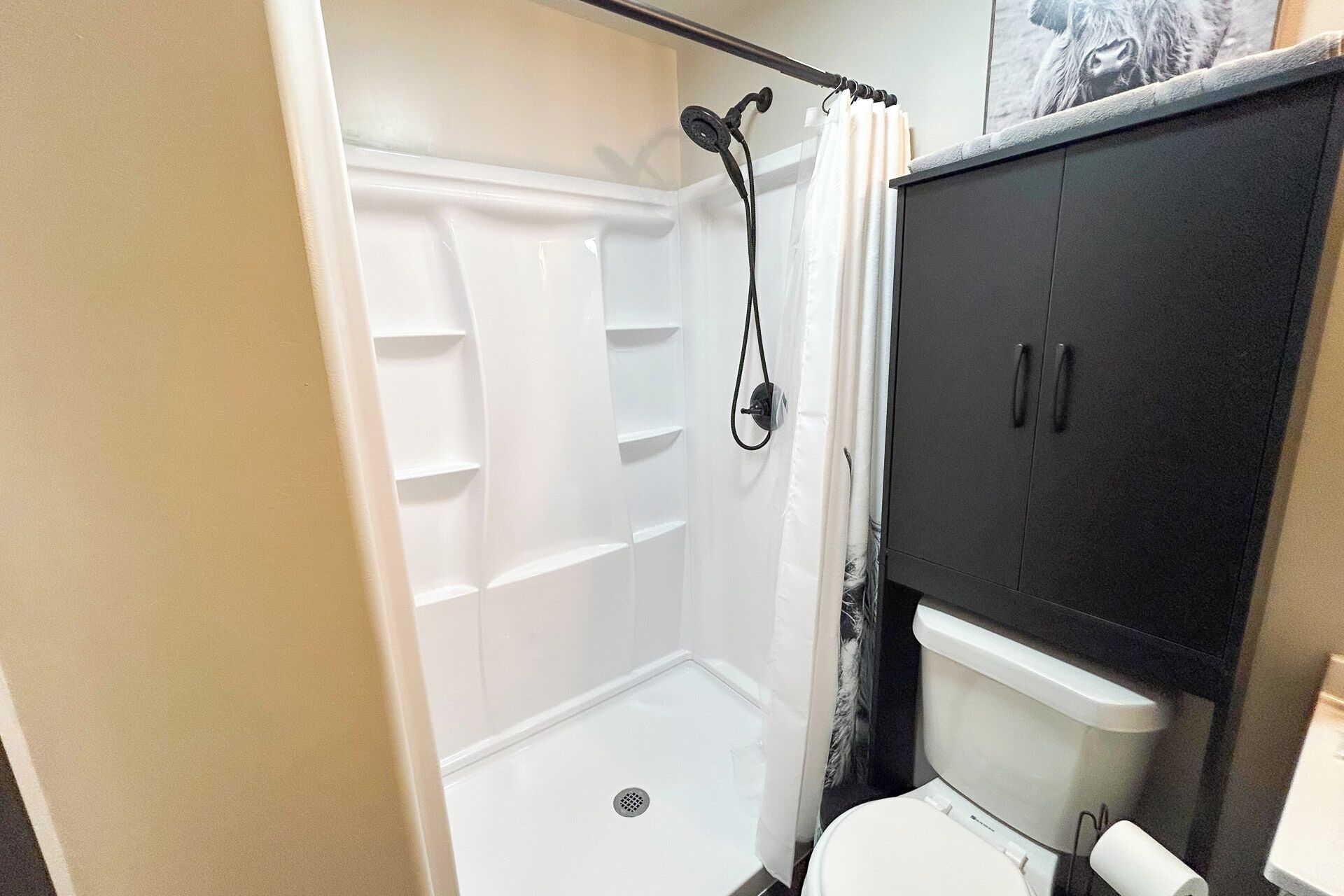 A bathroom with a shower, toilet, and dark-colored cabinet.