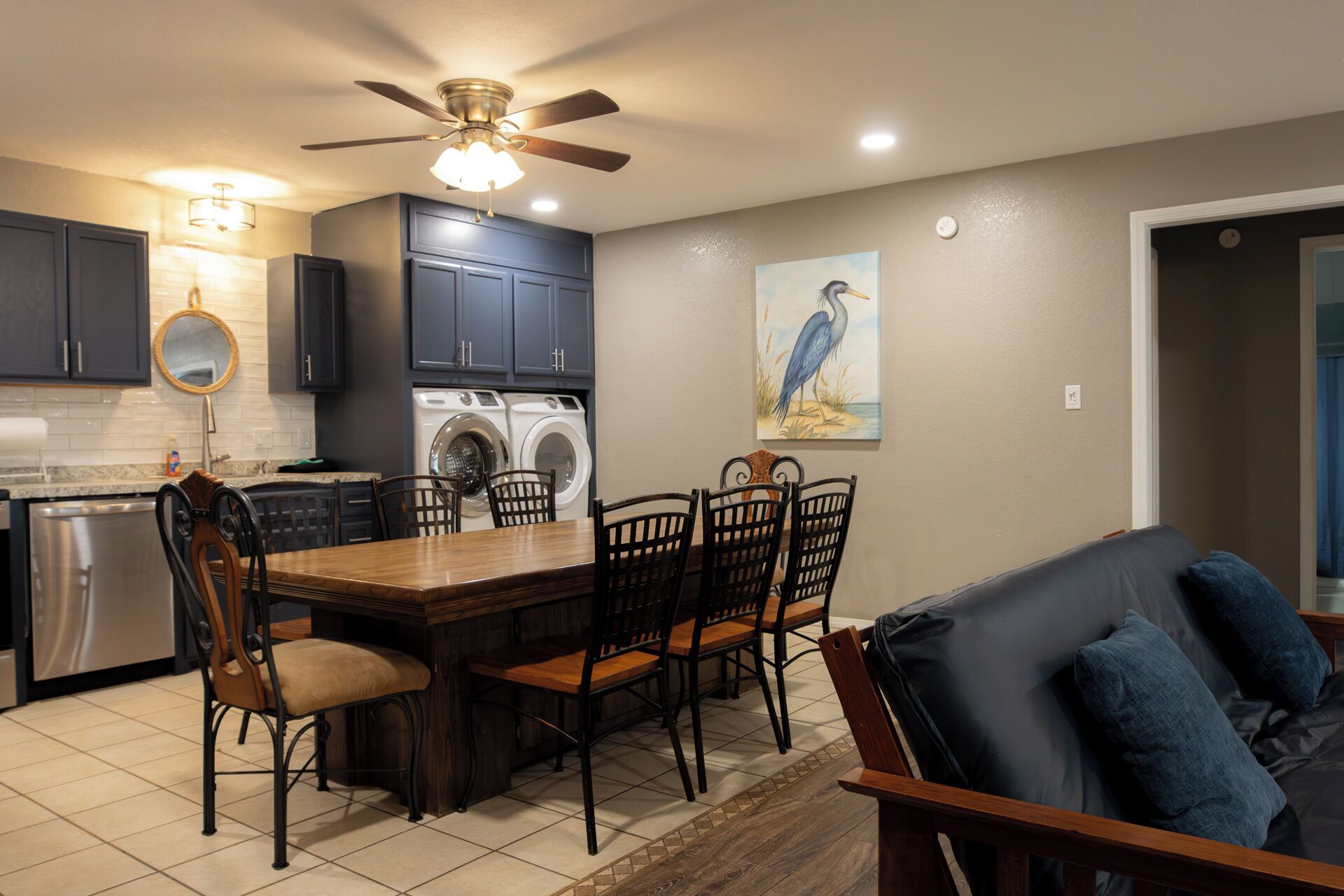 A modern kitchen with dark cabinets, a ceiling fan, and a dining area with a wooden table and chairs.