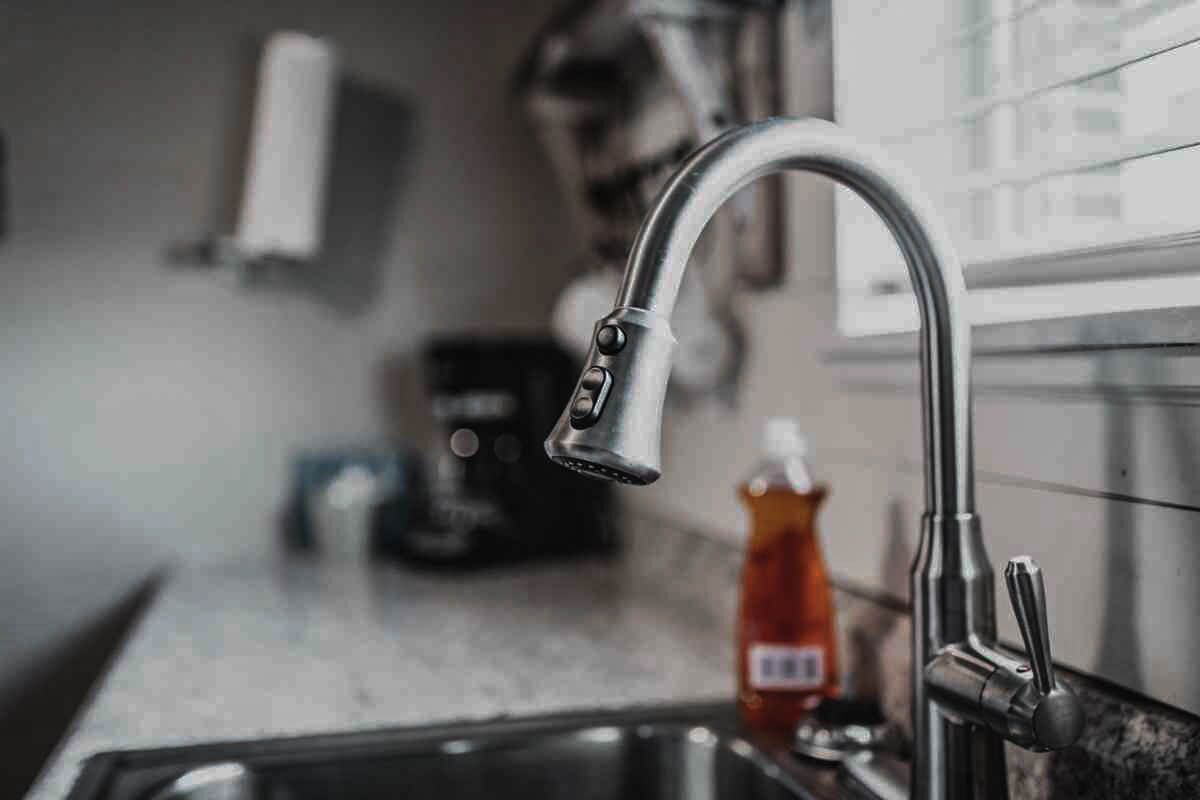 A kitchen sink with a modern faucet, a coffee maker, and a bottle of dish soap on the counter.