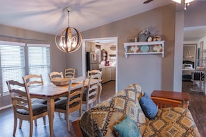Amplia sala de estar con una mesa y sillas de madera, un sofá estampado y una cocina al fondo.
