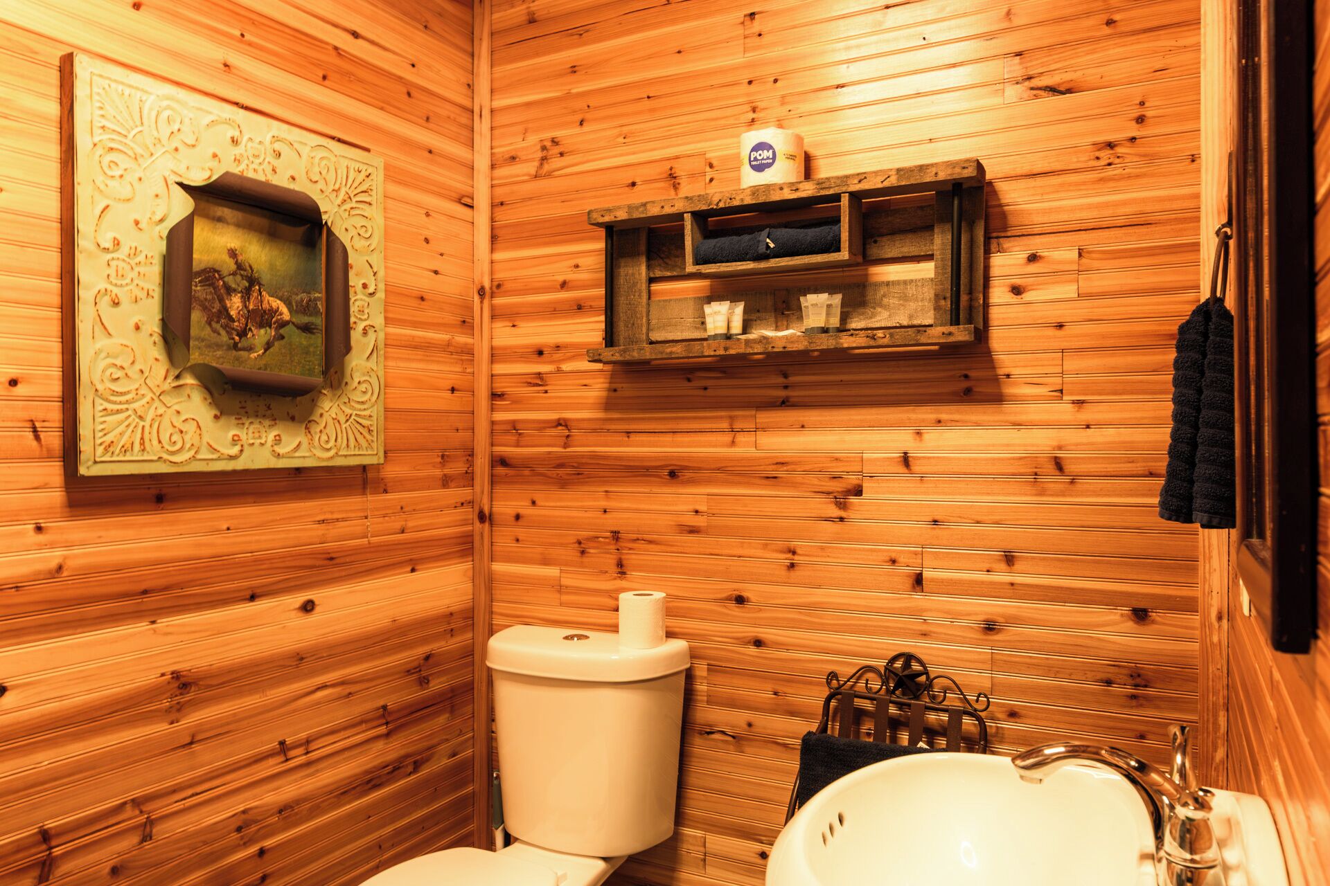 A wooden-paneled bathroom with a toilet, sink, and shelves with toiletries.