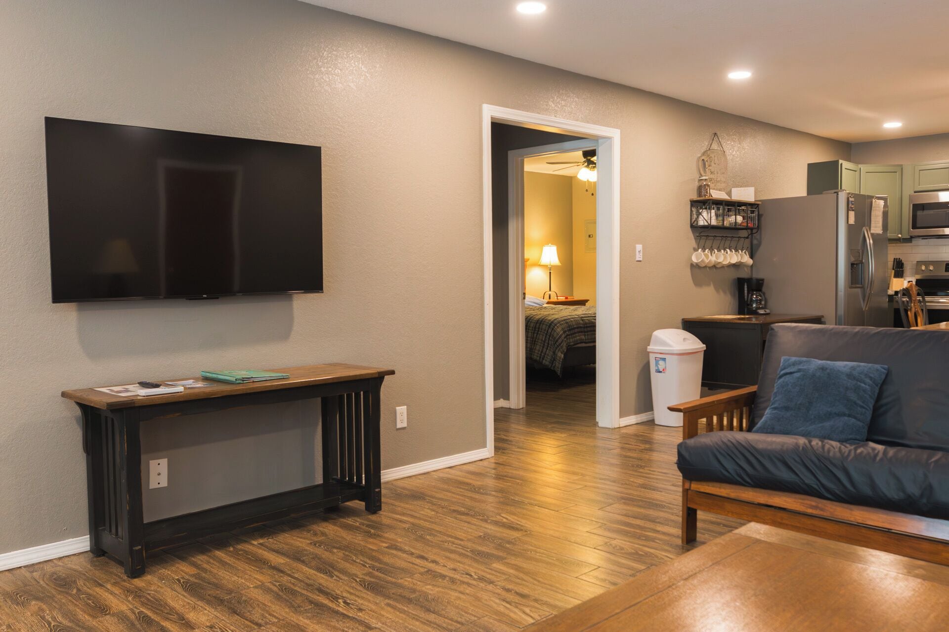 A living room with a flat-screen TV, a wooden console table, a sofa, and a kitchen area with a microwave and cabinets.