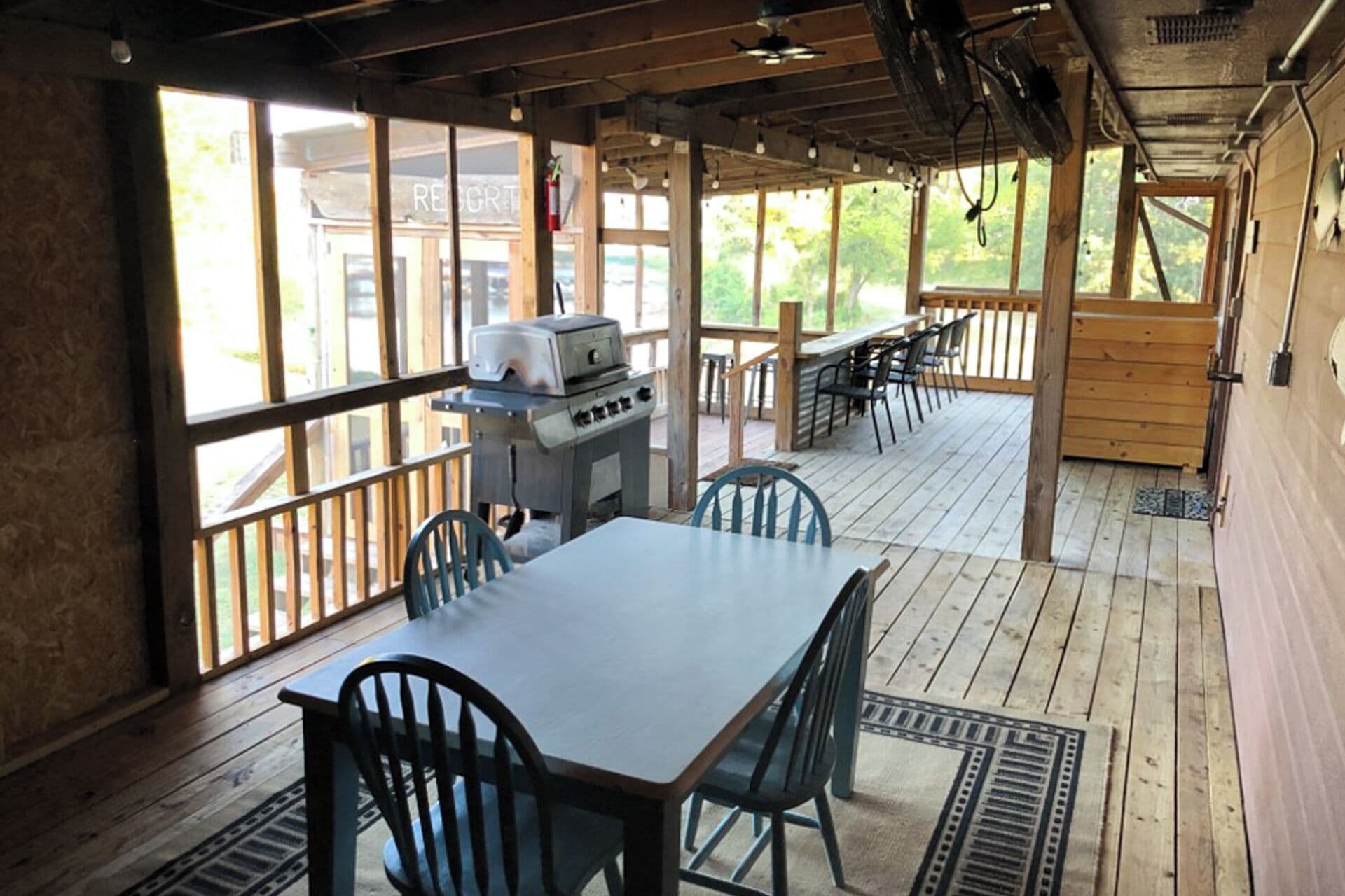 Un espacio comedor al aire libre cubierto, con una parrilla, mesas y sillas de madera.