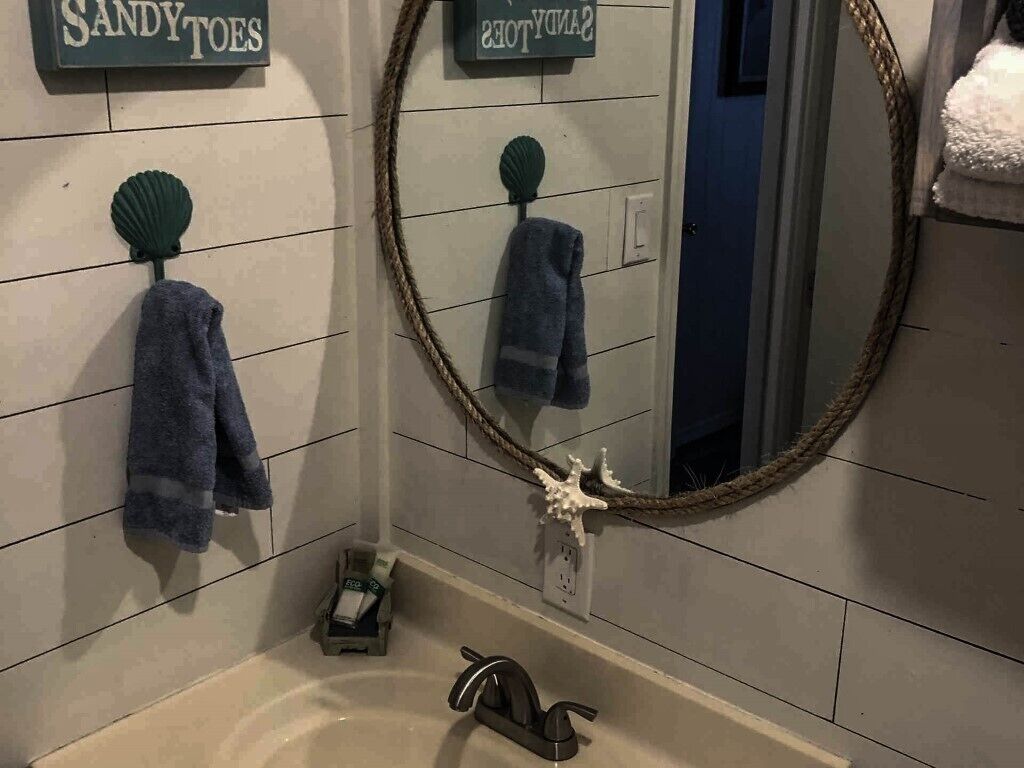 Un baño con lavamanos, dos toallas colgadas en ganchos, un espejo y una concha decorativa.
