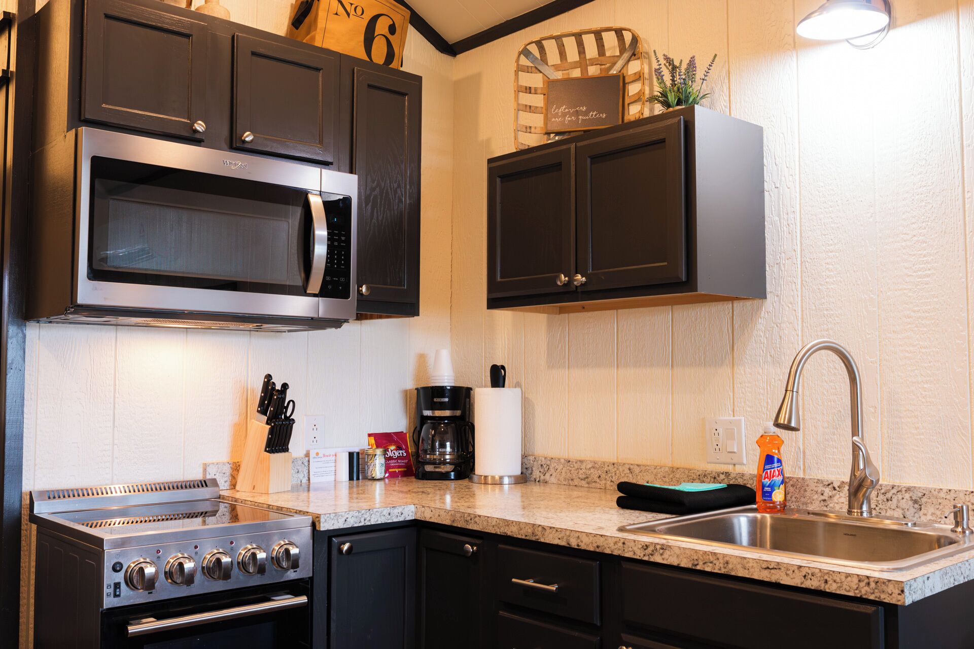 A kitchen with dark cabinets, a stainless steel stove, a microwave, and a sink with a faucet.