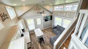 A spacious living area with a large window, a ceiling fan, and a flat-screen TV.