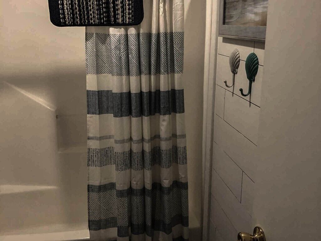 Un baño con cortina de ducha a rayas, un perchero con una toalla y una puerta con ventana.