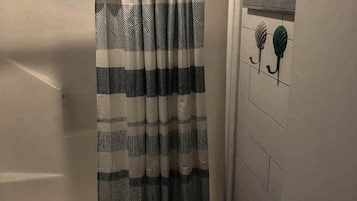 Un baño con cortina de ducha a rayas, un perchero con una toalla y una puerta con ventana.
