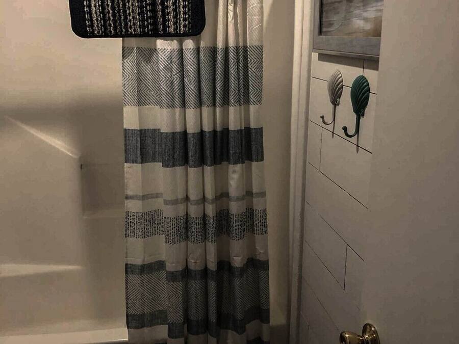 Un baño con cortina de ducha a rayas, un perchero con una toalla y una puerta con ventana.