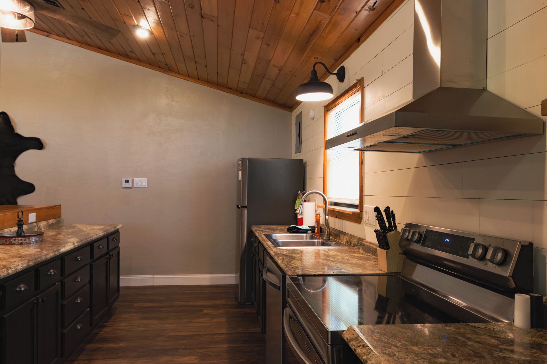 A modern kitchen with wooden ceiling beams, a stainless steel refrigerator, a double sink, and a built-in oven.