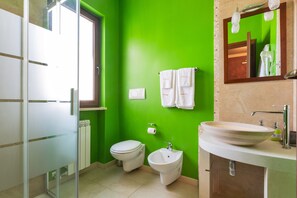 A bathroom with a green wall, a white sink, a bidet, and a toilet.