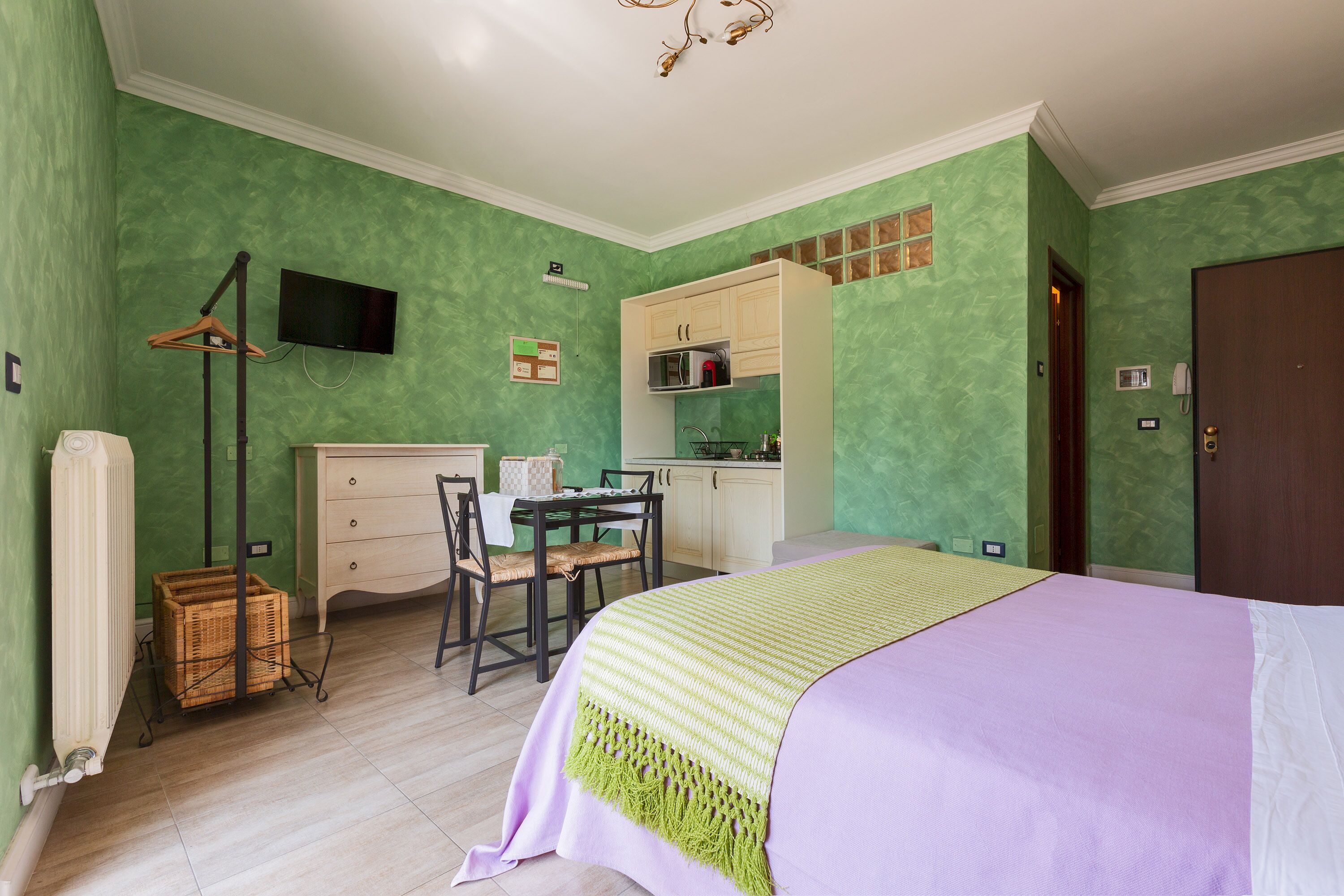 Een kamer met een bed, een bureau, een stoel, een televisie en een kitchenette.