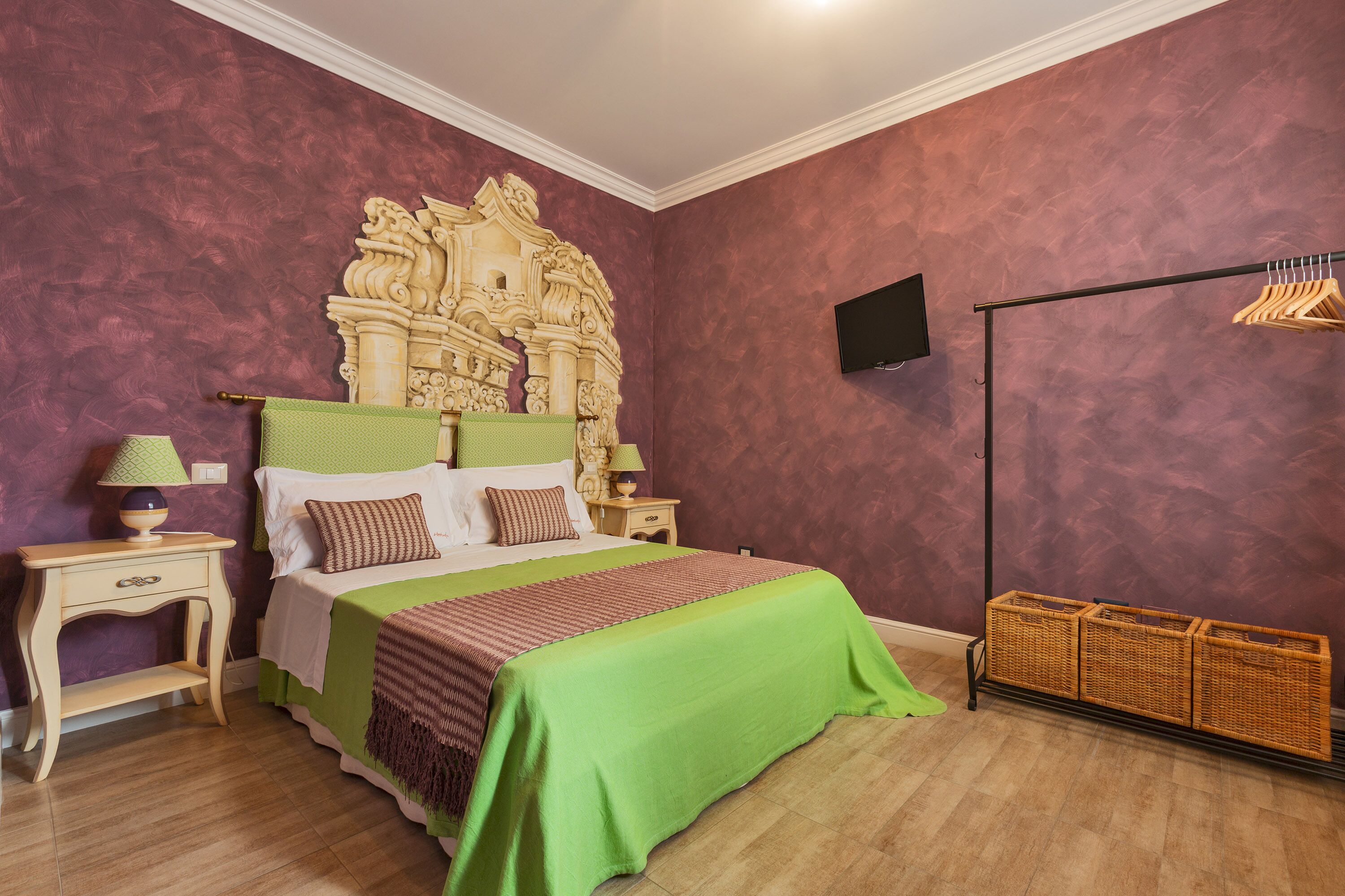 Ein Schlafzimmer mit einem großen Bett, einem Kopfteil mit aufwendigen Schnitzereien, einem an der Wand montierten Fernseher und einem Kleiderständer mit Kleiderbügeln.