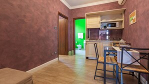 Cocina compacta con armarios de madera, un microondas y un comedor con mesa y sillas.