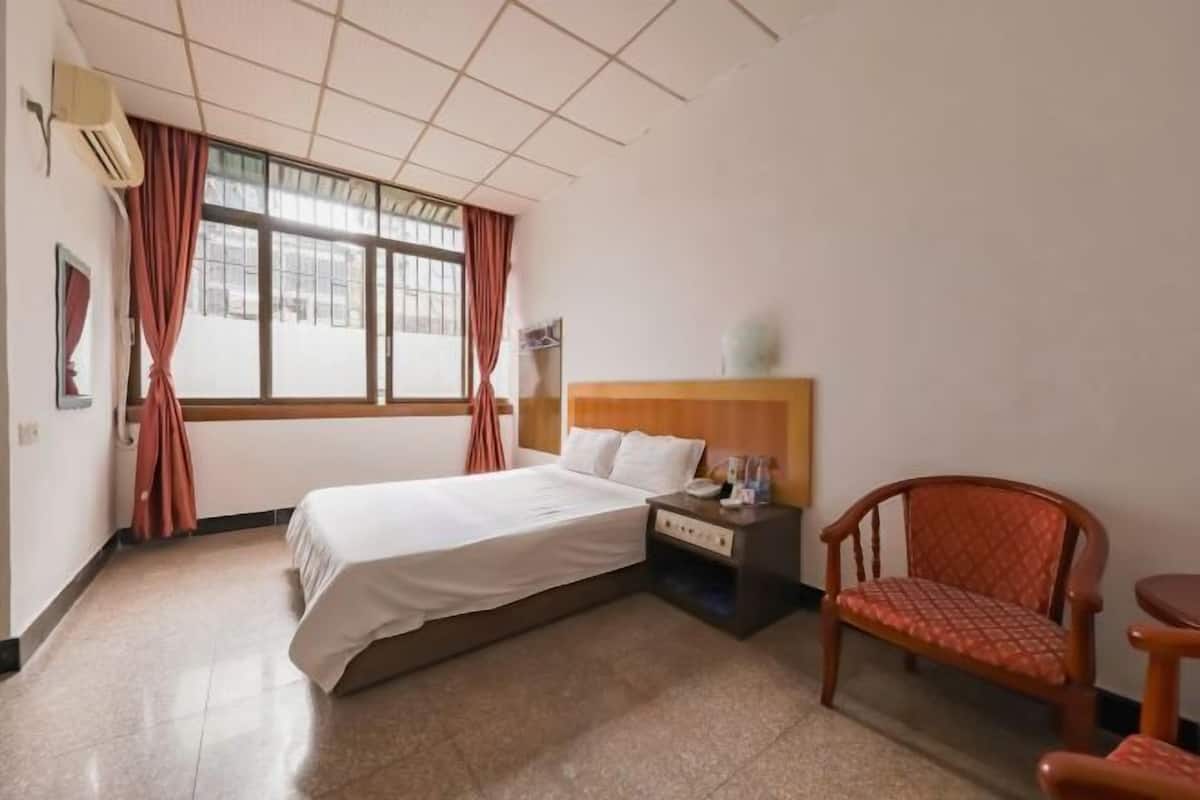 A hotel room with a bed, a nightstand, a chair, and a window with curtains.