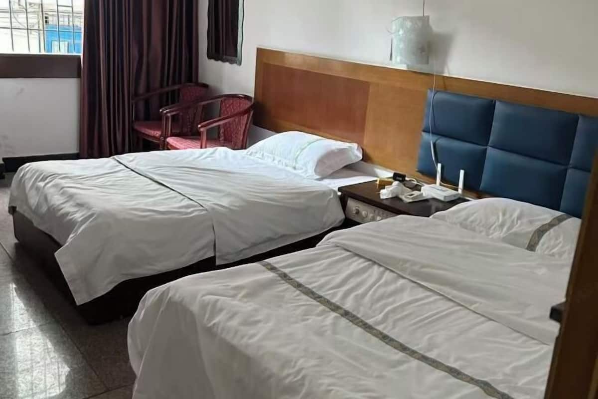 A hotel room with two beds, a wooden headboard, a small table with a lamp, and a chair.