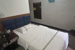 Una habitación de hotel con una cama, cabecero de madera, mesita de noche, escritorio y panel de control en la pared.