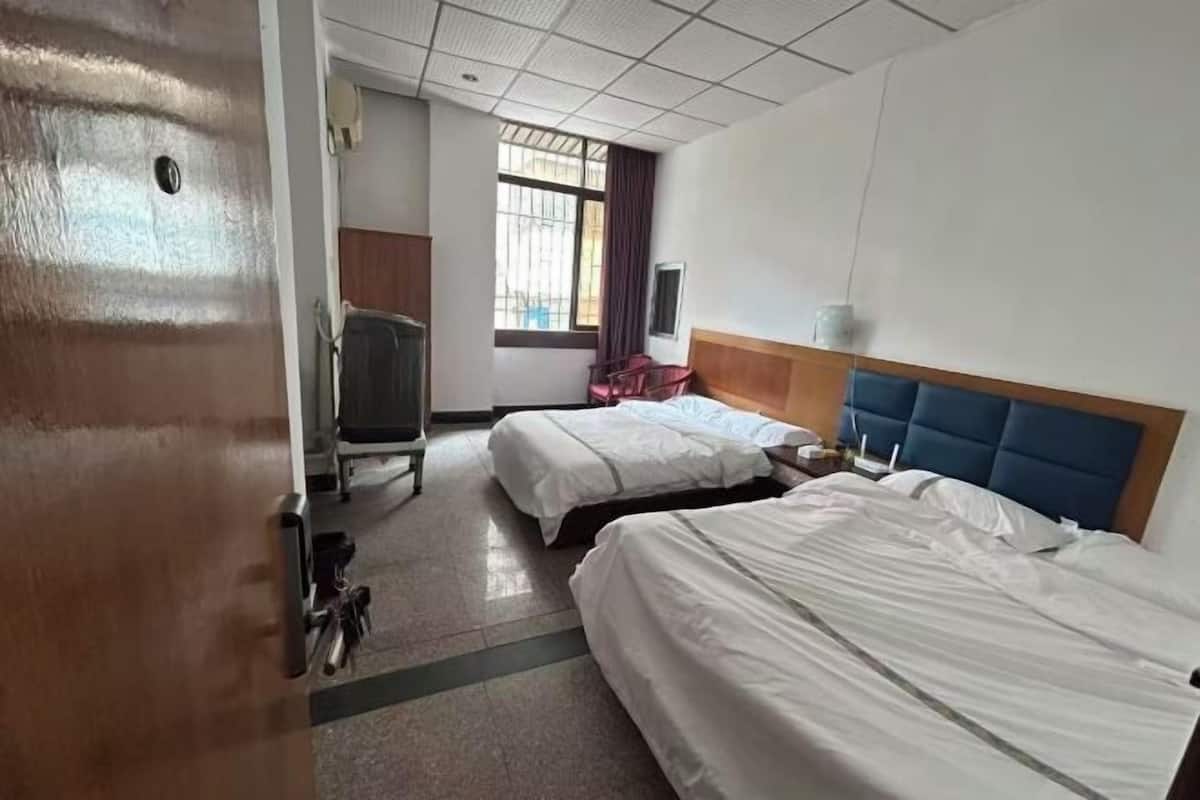 A hotel room with two beds, a desk, a chair, a window with curtains, and a door.