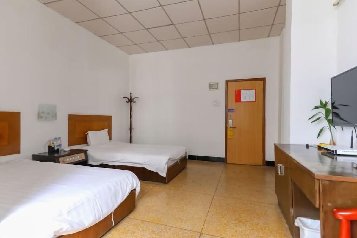 A hotel room with two beds, a desk with a computer, a TV, and a door with a sign.