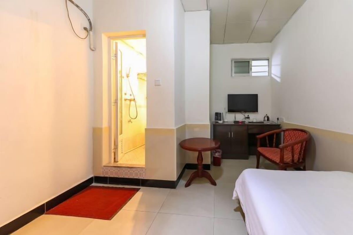 A hotel room with a bed, a desk, a chair, a TV, and a shower area.