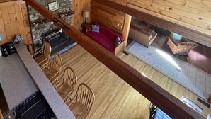 A wooden cabin interior with a dining area, kitchen, and a cozy living space with a fireplace. - Good Times Chalet Limit 19 5 Bedroom Chalet by RedAwning (Bridgton)