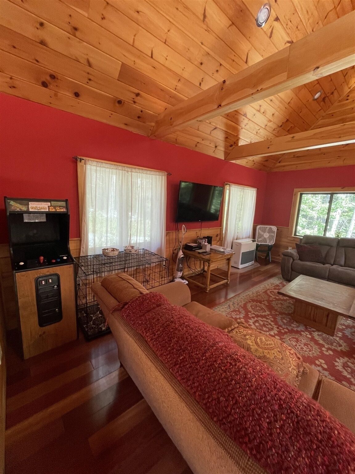 A cozy living room with a wooden ceiling, a red wall, a sofa, a television, and a fireplace.