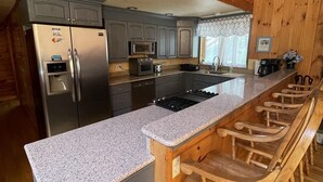 A kitchen with a granite countertop, wooden bar stools, and a stainless steel refrigerator. - Good Times Chalet Limit 19 5 Bedroom Chalet by RedAwning (Bridgton)