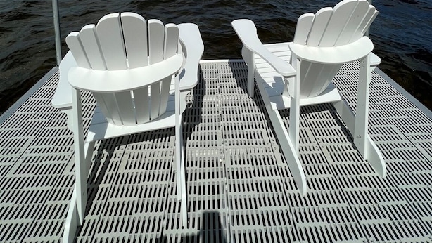 Två vita Adirondack-stolar står på ett metallräcke med utsikt över havet och en delvis molnig himmel.