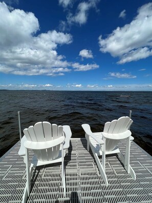 Two white Adirondack chairs on a metal deck with a view of the ocean and a partly cloudy sky. - Camp Carroll Limit 6 3 Bedroom Home by RedAwning (Sebago)