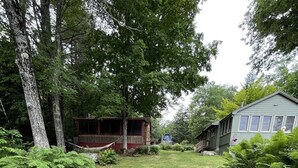 A grassy yard with a wooden cabin and a house. - Greens Limit 6 2 Bedroom Cottage by RedAwning (Sebago)