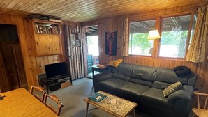 A cozy cabin interior with a wooden ceiling, a sofa, a coffee table, and a dining table with chairs. - Greens Limit 6 2 Bedroom Cottage by RedAwning (Sebago)