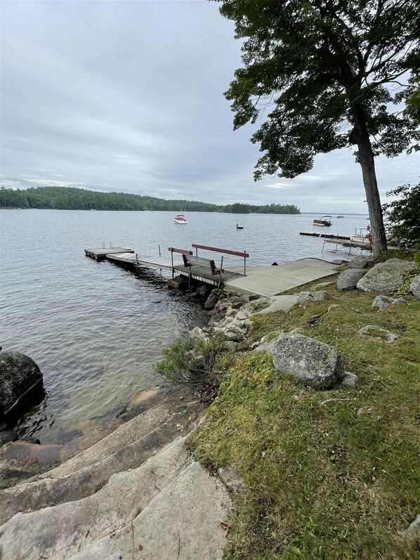 Une jetée au bord du lac avec un bateau, une zone herbeuse parsemée de rochers et un arbre.