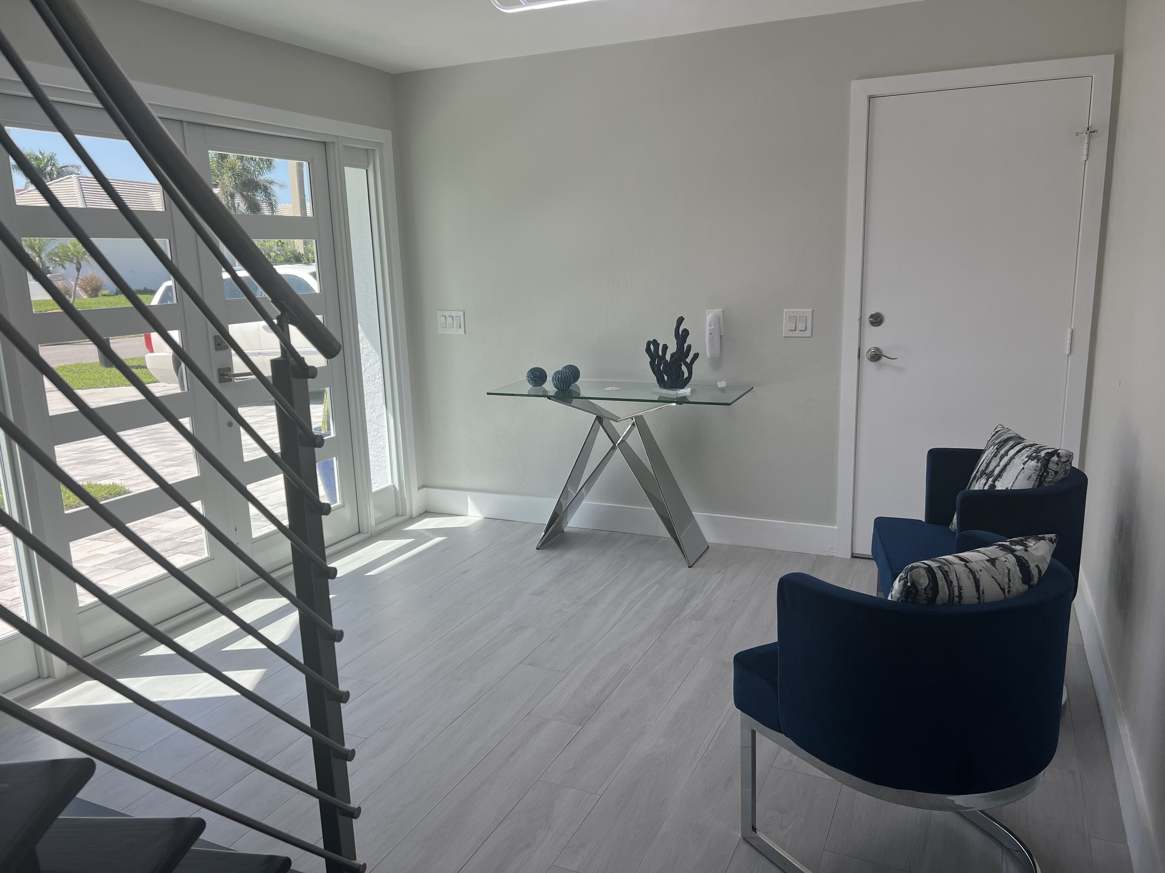 A modern living room with a glass coffee table, a blue armchair, and a white door.