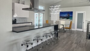 Una cocina moderna con una isla central, taburetes de bar y un comedor con mesa y sillas.