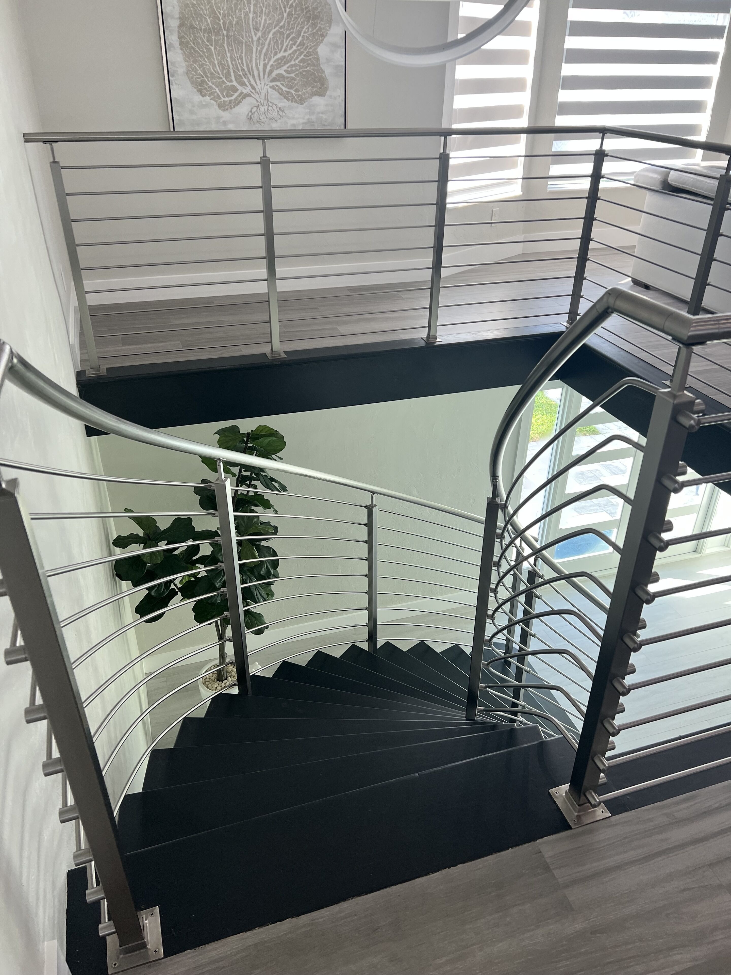 A modern spiral staircase with metal railings and a potted plant on the landing.