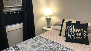 Un dormitorio con cama, lámpara de noche, calentador y ventana con cortinas.
