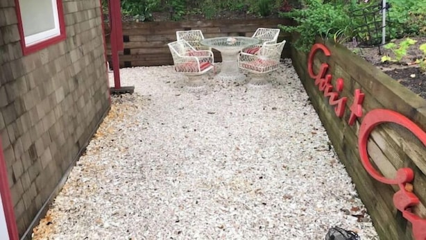 Un pequeño espacio al aire libre con sillas de mimbre y una mesa, rodeado por un camino de grava y una valla de madera.