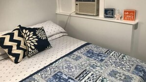 Un dormitorio con cama, almohadas, colcha, aire acondicionado y dos letreros en la pared.