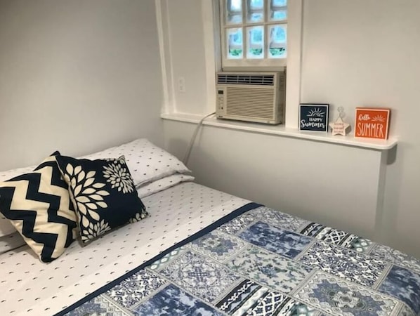 Une chambre à coucher avec un lit, des oreillers, une couette, un climatiseur et deux panneaux affichés sur le mur.