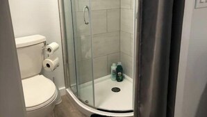 Un baño con ducha de vidrio, inodoro y un pequeño lavabo con artículos de aseo.