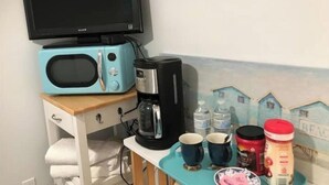 Una kitchenette equipada con microondas, cafetera y una pequeña mesa con tazas y recipientes.