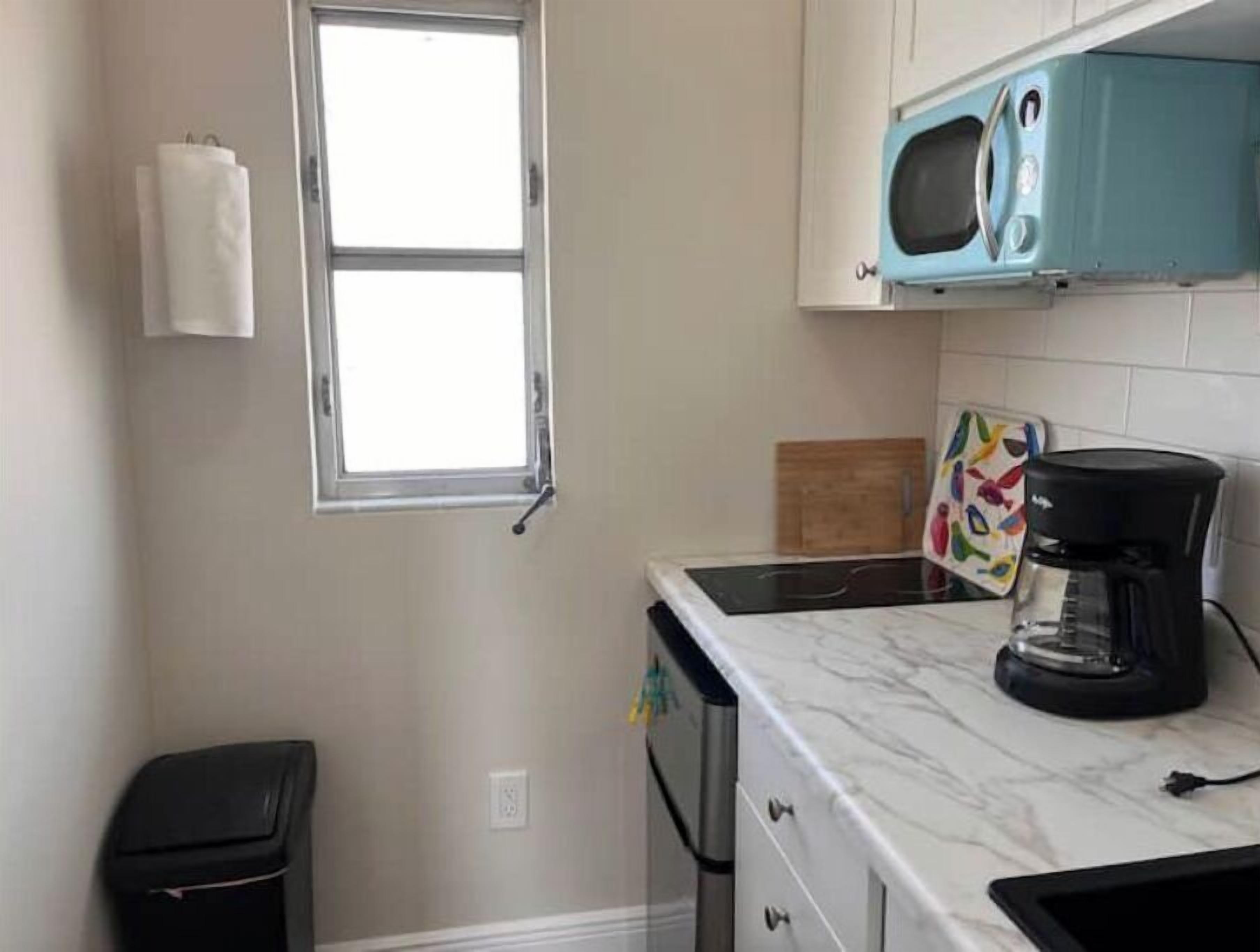 Una cocina compacta con microondas, cafetera y un ventanal pequeño.