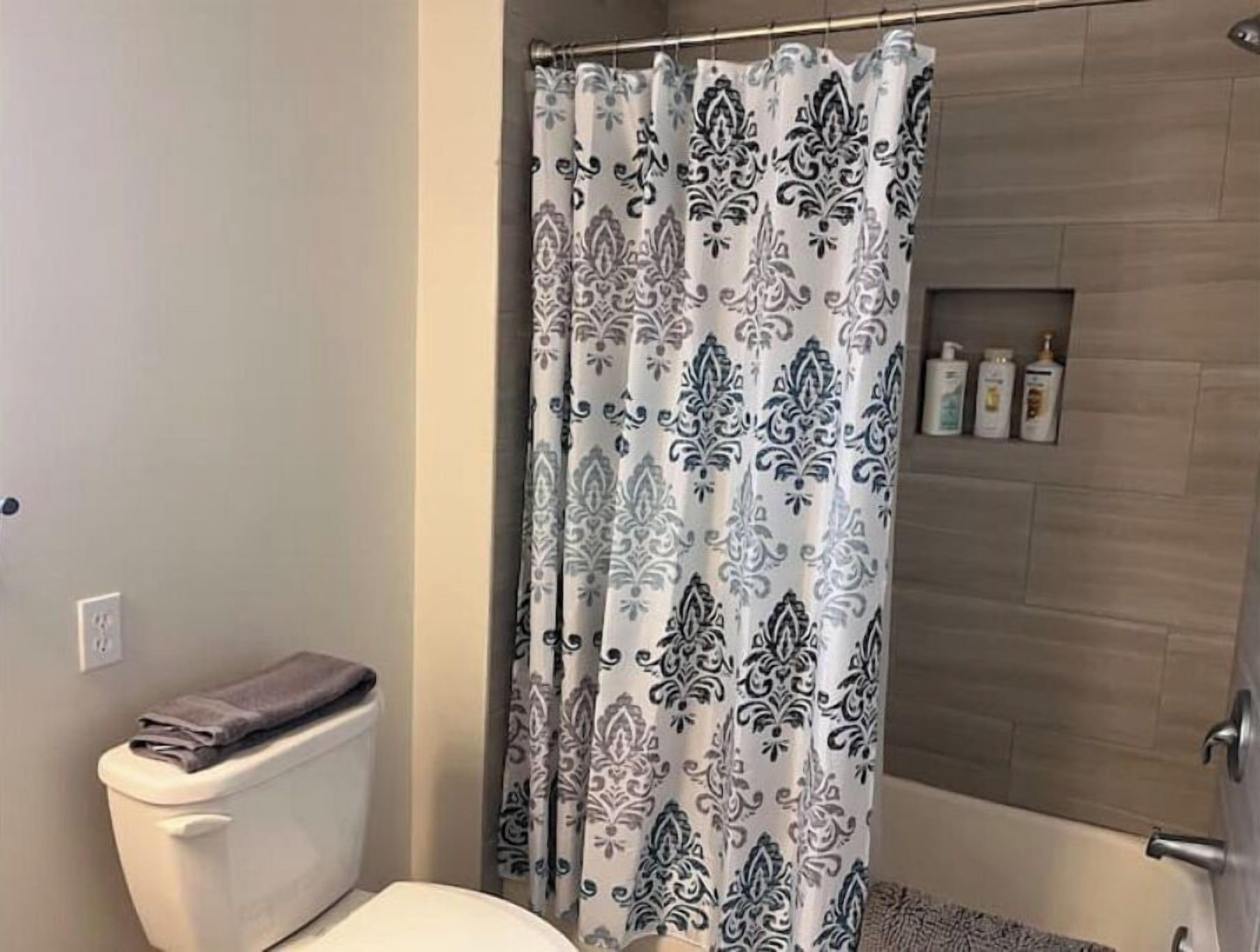 A bathroom with a toilet, a shower curtain with a floral pattern, and a shelf with toiletries.