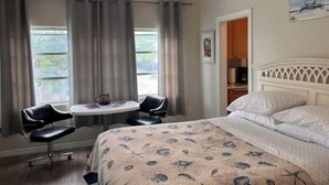 Et hotelværelse med en seng, et skrivebord med to stole, en ventilator i loftet og et billede på væggen.
