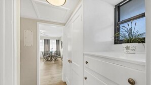 Un couloir doté d’un plancher en bois, de murs blancs et d’une fenêtre où est posée une plante.