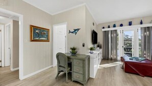Une pièce avec un plancher en bois, un bureau avec des tiroirs, une chaise, un canapé rouge, un téléviseur et une fenêtre avec des rideaux.