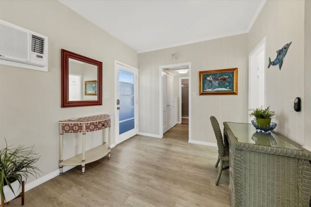 A dining area with a glass table, wicker chairs, a console table with a patterned top, and a painting on the wall.