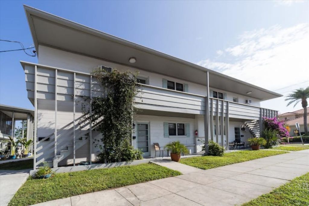 A modern two-story building with a flat roof, large windows, and a covered outdoor area with a staircase.