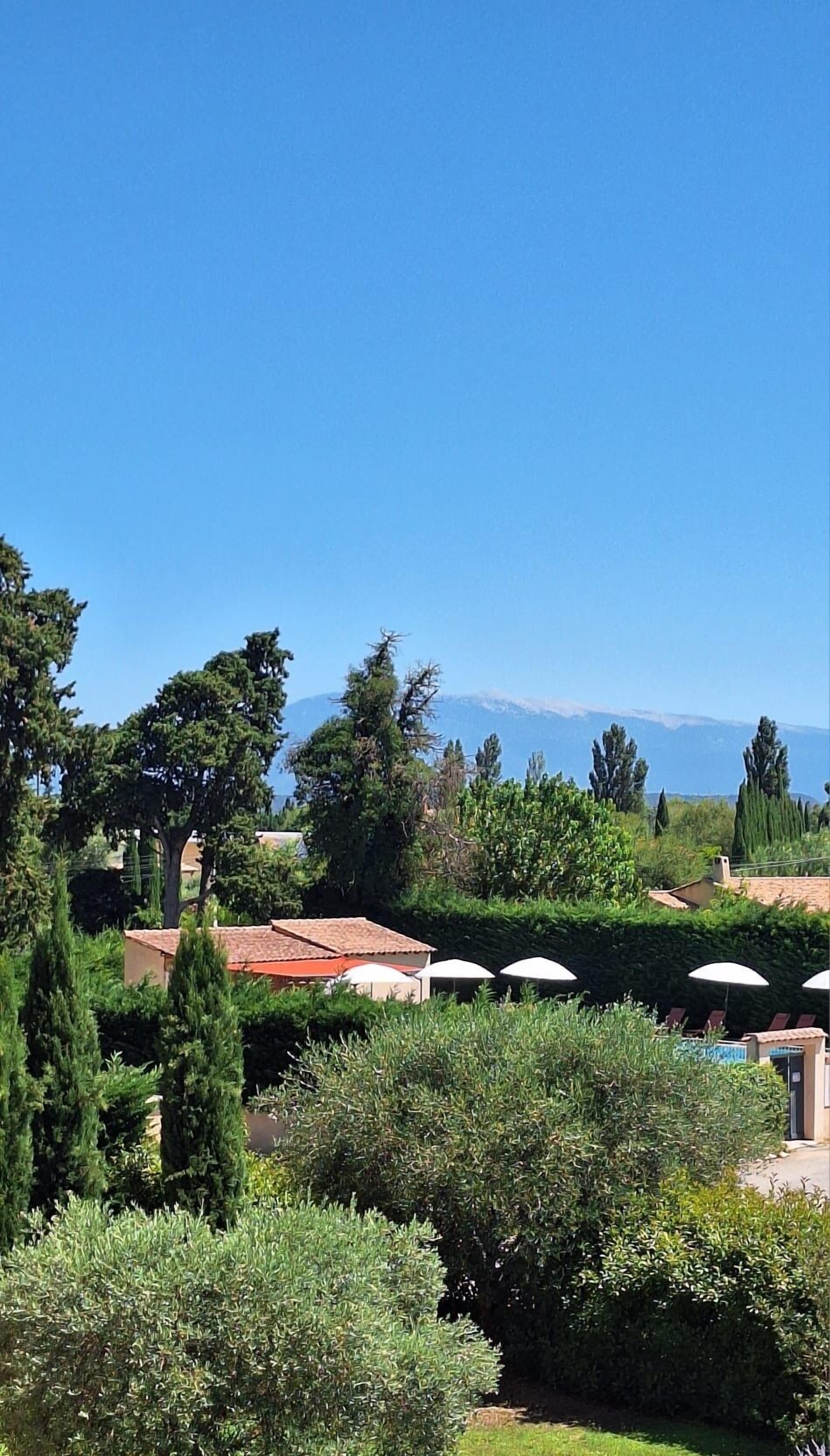 A view of a property with a pool, umbrellas, and a mountainous backdrop.