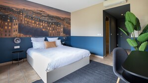Ett hotellrum med en stor säng, ett litet bord, en stol och ett stort fönster med utsikt över staden.